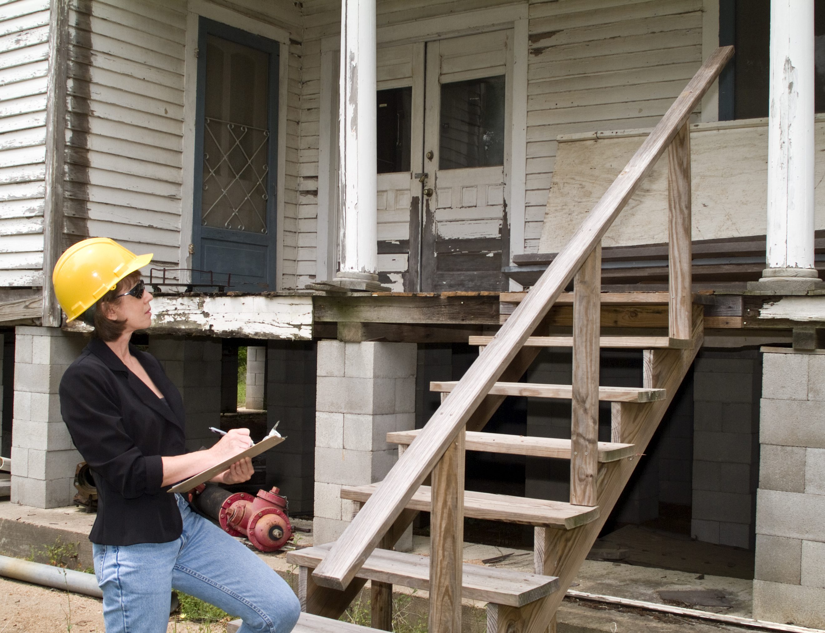 Inspector evaluating old house with clipboard.