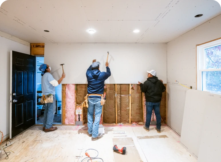 Workers installing drywall in a room.